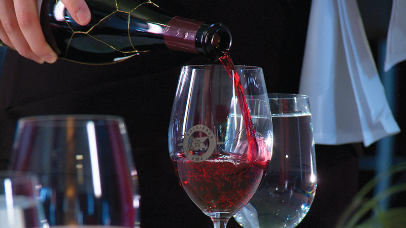 A close-up of a waiter pouring red wine into a glass.