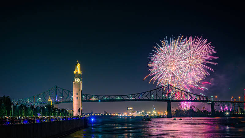  Une vue nocturne spectaculaire d'un feu d'artifice illuminant le ciel au-dessus d'un pont emblématique et d'une tour horloge, avec des lumières urbaines scintillantes et une rivière calme au premier plan.