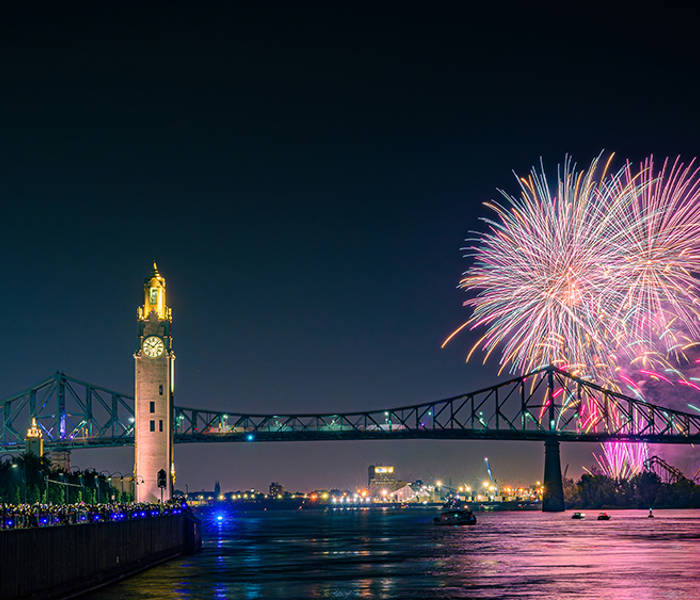  Une vue nocturne spectaculaire d'un feu d'artifice illuminant le ciel au-dessus d'un pont emblématique et d'une tour horloge, avec des lumières urbaines scintillantes et une rivière calme au premier plan.