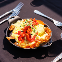 Cassolette gourmande comprise dans le brunch avec œufs brouillés, pommes de terre grelots, poivrons rôtis, fromage en grains, bacon, saucisses et sauce hollandaise accompagnée d'un verre de mimosa 