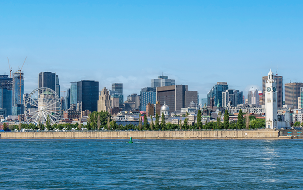 Vue sur la skyline de Montréal dans un ciel bleu en arrière plan et le fleuve Saint-Laurent scintillant au premier plan.