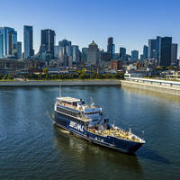 A cruise ship sailing on a river, with a panoramic view of a city skyline featuring tall skyscrapers in the background under a clear sky.