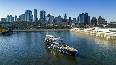 Un bateau de croisière naviguant sur une rivière, avec une vue panoramique sur une ville avec de hauts gratte-ciels en arrière-plan sous un ciel dégagé.