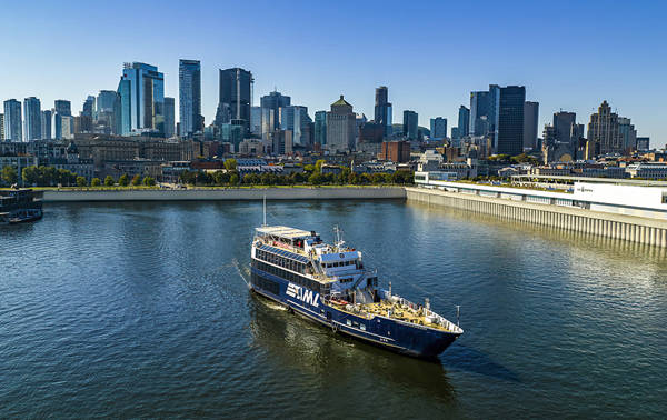 Un bateau de croisière naviguant sur une rivière, avec une vue panoramique sur une ville avec de hauts gratte-ciels en arrière-plan sous un ciel dégagé.