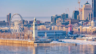 Vue panoramique sur le Vieux-Port de Montréal en hiver, avec la Tour de l’Horloge, la grande roue et les bâtiments du centre-ville sous un ciel clair.