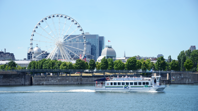 La navette fluviale naviguant sur le Saint-Laurent avec la grande roue de Montréal en arrière plan.