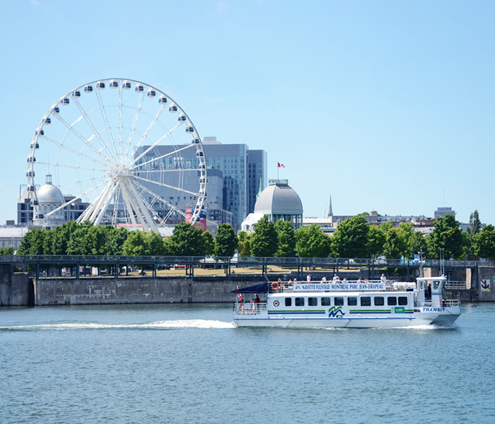 La navette fluviale naviguant sur le Saint-Laurent avec la grande roue de Montréal en arrière plan.