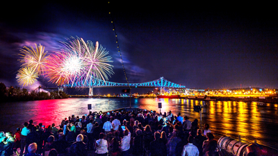 Une foule profite d’un feu d’artifice vibrant depuis la terrasse principale du AML Cavalier Maxim à Montréal avec vue sur le Pont Jacques Cartier et la ville illuminés en arrière plan.