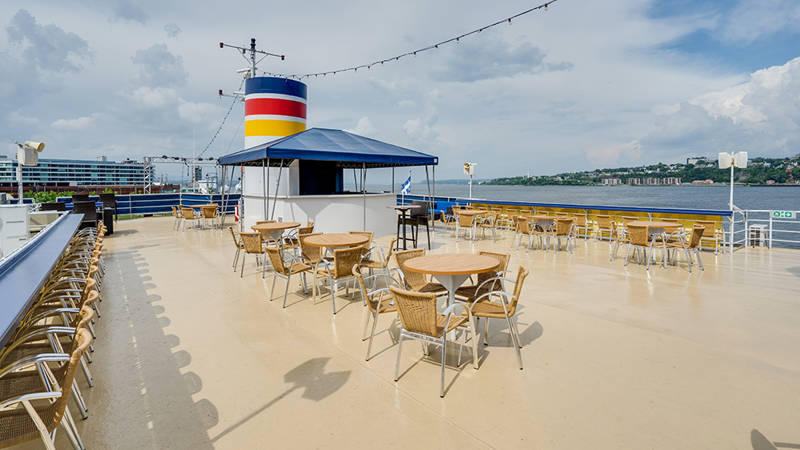 Terrasse extérieur du pont supérieur du navire AML Louis Jolliet avec des tables et des chaises à la disposition des clients à Québec avec vue sur le fleuve Saint-Laurent 