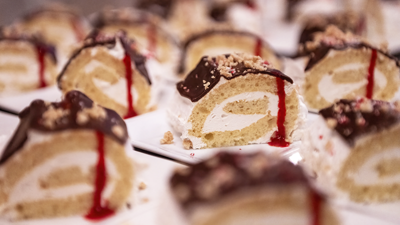 Delicious small logs with a cream filling, topped with chocolate and raspberry sauce, sprinkled with crushed nuts, ready to be served.