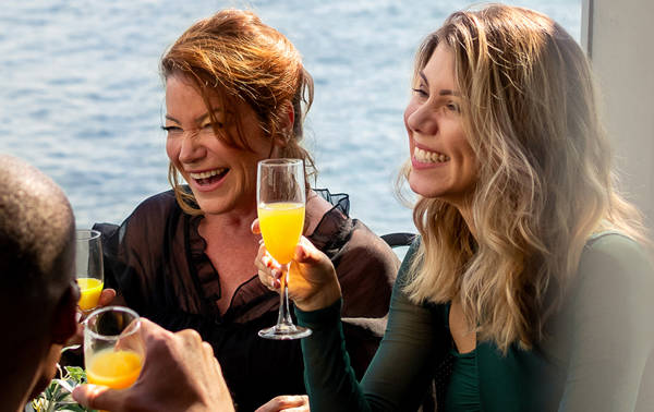 Un groupe d'amis partage un moment convivial dans un restaurant lumineux, une femme souriante tient un verre de mimosa à la main.