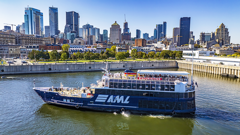 Vue aérienne du navire AML Cavalier Maxim stationné dans le Vieux-Port de Montréal de jour avec vue sur la skyline de la ville en arrière plan.